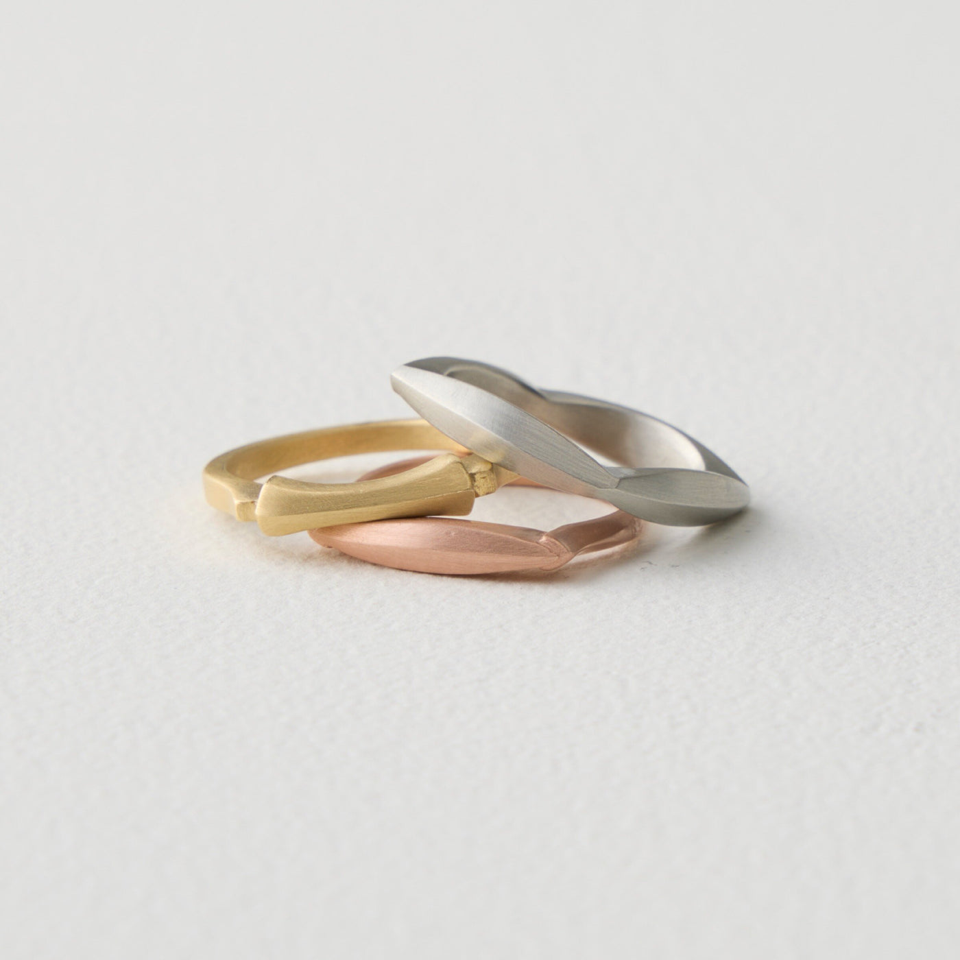 stacked top to bottom: Four Allonge Band in 18k white gold, Hourglass Stacking Ring in 18k yellow gold, Allonge Stacking Ring in 18k rose gold